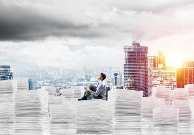 Düşünceli işadamı uzak belgeler cityscape ve arka plan üzerinde güneş ışığı ile yığını üzerinde otururken arıyorum. Karışık teknik.