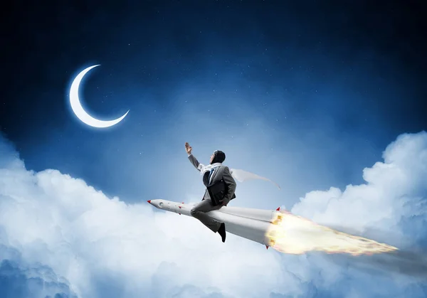 蓝夜影像 中的年轻商人的概念形象与云和月亮的背景下的火箭飞行 — 图库照片