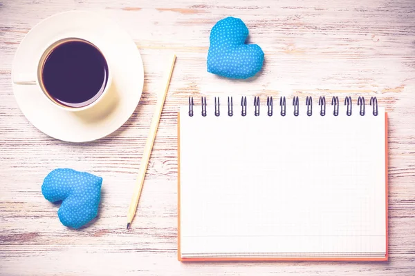 Coffee cup notepad pencil and two hearts on wooden surface