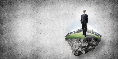 Yeşil yüzen adada beton zemine karşı duran kendine güvenen zarif iş adamı.