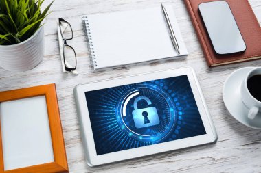 Ofis eşyalarıyla iş yeri ve ekranda asma kilit simgeleri olan tablet