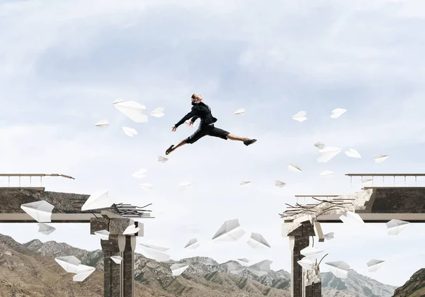 商业妇女跳过桥梁之间的差距在飞行纸飞机作为克服挑战的标志 背景上的影像和自然观 — 图库照片