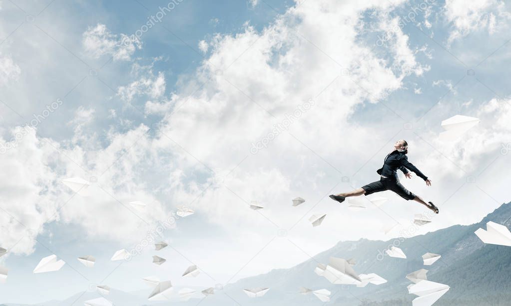 Attractive business woman in suit jumping in the air among flying paper planes as symbol of active life position. Skyscape and nature view on background. 3D rendering.