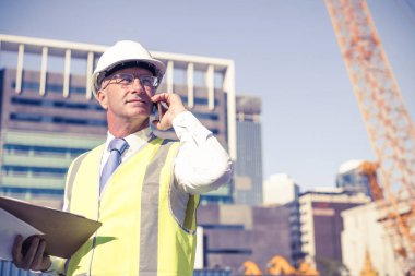 Kıdemli mühendis kostümlü ve kasklı konuşan cep telefonu.