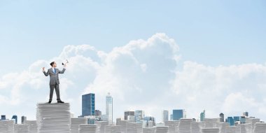 İşadamı hoparlör belgelerle yığını üzerinde elinde duran arka planda gökyüzü ve şehir manzaralı takım elbiseli. Karışık teknik.