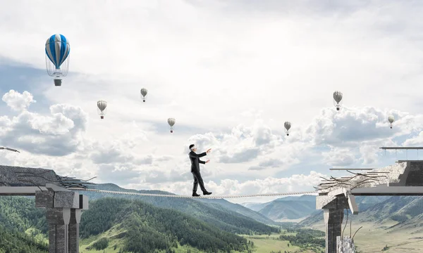 Businessman walking blindfolded on rope above huge gap in bridge as symbol of hidden threats and risks. Flying balloons and nature view on background. 3D rendering.