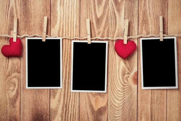 Instant photo frame and love hearts pinned to rope on wooden textured background