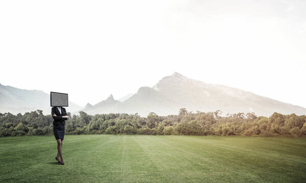 Business woman in suit with TV instead of head keeping arms crossed while standing on the road with beautiful landscape on background.