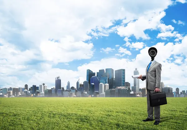 头戴相机的男子站在绿草之上，与现代城市景观相抗衡 — 图库照片