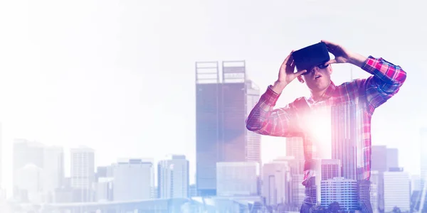 Young man with virtual reality headset or 3d glasses over cityscape background