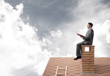 Elinde kırmızı kitap ile ev oturan takım elbiseli genç işadamı