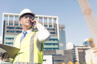 Kıdemli mühendis kostümlü ve kasklı konuşan cep telefonu.