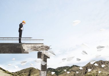 Genç takım elbiseli mühendis ve arka plan üzerinde hava ve Doğa Manzaralı kırık köprüde kağıt uçak uçan arasında duran bakıyordu kask. 3D render.