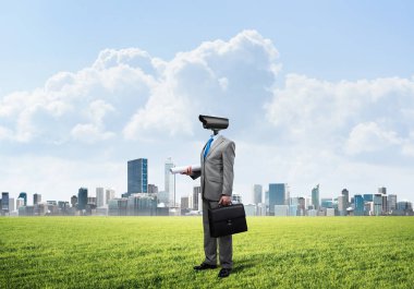 Modern şehir manzarasına karşı yeşil çimlerin üzerinde duran kamera başlı adam.