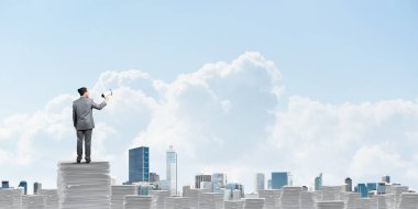 İşadamı hoparlör belgelerle yığını üzerinde elinde duran arka planda gökyüzü ve şehir manzaralı takım elbiseli. Karışık teknik.