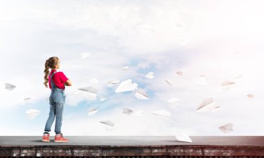 Sevimli kız etrafında uçan çatı ve kağıt uçaklar binasında ayakta