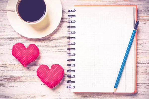 Coffee cup notepad pencil and two red hearts on wooden surface