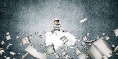 Genç küçük çocuk gözleri koruma kapalı ve seyir üzerinde uçan bulut kitaplar ile gri karanlık duvar arka plan üzerinde uçan arasında meditasyon sırasında konsantre.