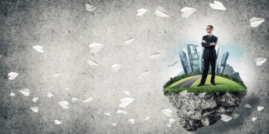 Yeşil yüzen adada beton zemine karşı duran kendine güvenen zarif iş adamı.