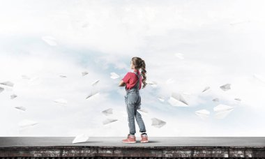 Sevimli kız etrafında uçan çatı ve kağıt uçaklar binasında ayakta