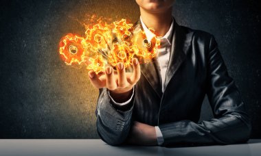 İşadamı ile arka plan üzerinde koyu duvar elinde sunan yanan cogwheels yapısı uygun.