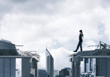 Gizli tehditlerin ve risklerin sembolü olarak beton köprüde gözü kapalı yürüyen bir iş adamı. Arka planda şehir manzarası. 3B görüntüleme.