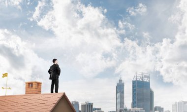 Kararlı genç işadamı evin çatısında dikiliyor ve başka tarafa bakıyor. Karışık ortam