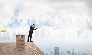 Çatıda takım elbiseli genç bir işadamı var. Karışık ortam