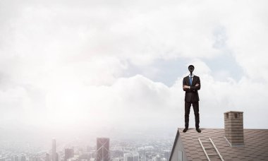 Evin çatısında baş durmak yerine kamerayla zum yapan yüzü olmayan bir iş adamı.