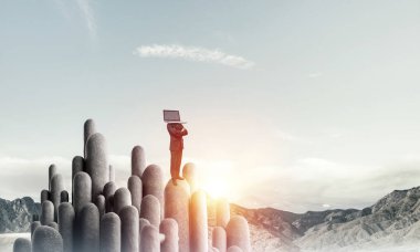 Arka plan üzerinde duran güzel gökyüzü ile taş sütun üst dizüstü bilgisayar kafasına silah tutmak yerine ile takım elbiseli işadamı geçti.