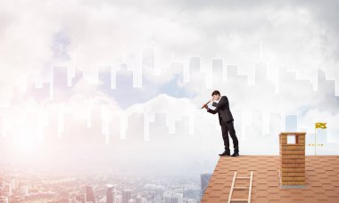 Çatıda takım elbiseli genç bir işadamı var. Karışık ortam