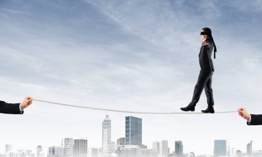 Gözlerinde perde olan bir iş adamı şehrin arka planında ipte yürüyor.