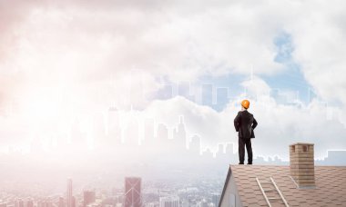 Takım elbiseli genç işadamı ve çatıda kask var. Karışık ortam