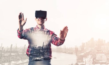 Sanal gerçeklik kulaklığı olan genç bir adam ya da şehrin arka planında 3 boyutlu gözlüklü.