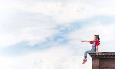 Üstte oturan ve bir şeyi işaret eden sevimli bir kız.