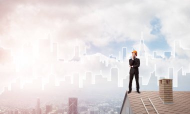 Takım elbiseli genç işadamı ve çatıda kask var. Karışık ortam