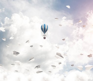 Kağıt uçakların arasında ve mavi bulutlu gökyüzünde renkli bir aerostat uçuyor. 3B görüntüleme.