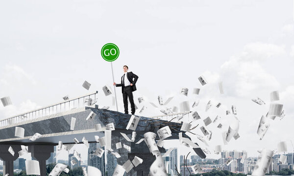 Confident businessman in suit holding green go sign while standing among flying papers on broken bridge with cityscape on background. 3D rendering.