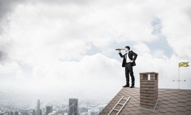 Genç kararlı işadamı çatının tepesinde dikilip dürbüne bakıyor. Karışık ortam