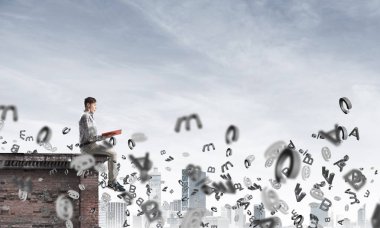 Elinde kırmızı kitap ile üst yapı üzerinde rahat oturan genç adam