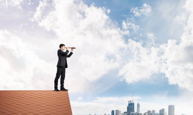 Genç kararlı işadamı çatının tepesinde dikilip dürbüne bakıyor. Karışık ortam