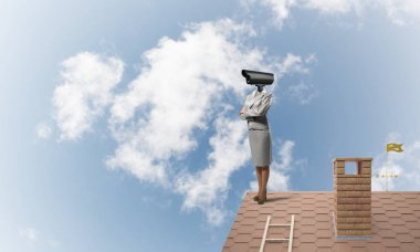 Evin çatısında baş durmak yerine kamerayla zum yapan yüzsüz iş kadını.