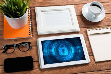 Ofis eşyalarıyla iş yeri ve ekranda asma kilit simgeleri olan tablet