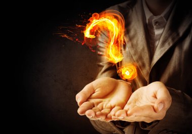 İşadamı artalanları karanlık duvara ile onun ellerinde yanan soru işareti sunan takım elbiseli Resim kırpılmış.