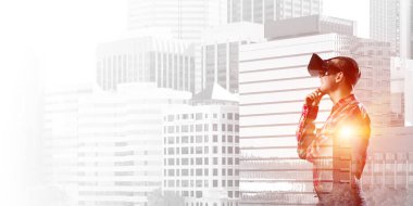 Sanal gerçeklik kulaklığı olan genç bir adam ya da şehrin arka planında 3 boyutlu gözlüklü.