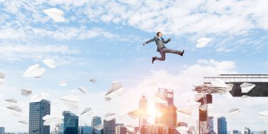 Kağıt uçaklar beton bridge uygulamasında zorlukların üstesinden sembolü olarak uçan ile gap üstünden atlayarak iş adamı. Cityscape zemin üzerine güneş ışığı ile. 3D render.