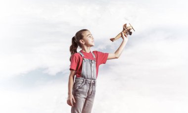 Elinde retro uçak modeliyle tulumlu şirin bir kız çocuğu.