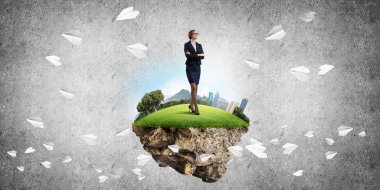 Yeşil yüzen adada beton zemine karşı duran kendine güvenen zarif bir iş kadını.