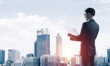 Elinde kağıtları olan genç ve zarif bir işadamı başka tarafa bakıyor.