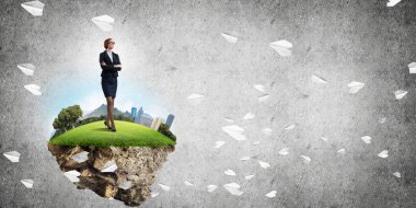 Yeşil yüzen adada beton zemine karşı duran kendine güvenen zarif bir iş kadını.